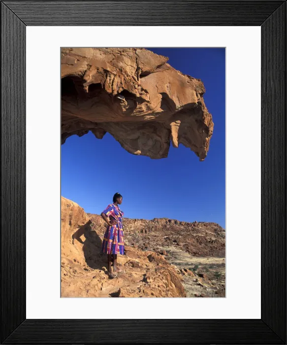 Framed Print : Namibia. African Woman standing under Red Rock formations, Twyfelfontein, Namibia, Africa Framed Print : Namibia. African Woman standing under Red Rock formations, Twyfelfontein, Namibia, Africa